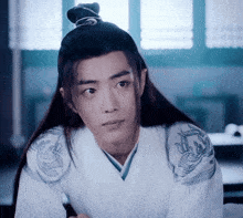 a young man with long hair and a bun on his head is wearing a white kimono .