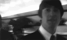 a black and white photo of a man in a suit and tie on a train .