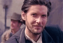 a close up of a man with a beard wearing a suit and hat .