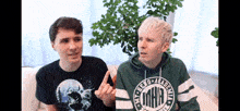 two men are sitting on a couch and one has a hoodie that says mha