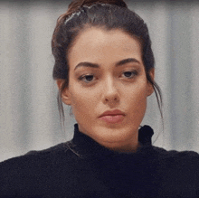 a close up of a woman 's face wearing a black turtleneck sweater and a bun .