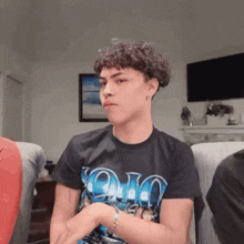 a young man with curly hair is wearing an ohio t-shirt while sitting on a couch .