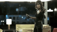 a woman in a black top and black pants is standing in a living room holding a gun .