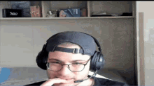 a man wearing headphones and a hat has a solo box on the shelf behind him