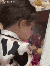 a little girl in a cow print shirt is looking at a doll in a box .