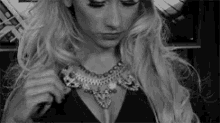 a woman with long blonde hair is wearing a necklace and a black dress .