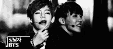 a black and white photo of two young men standing next to each other with a microphone in their mouths .