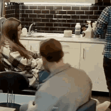 a man and a woman are sitting in a kitchen with a man spraying a bottle .