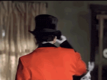 a man in a top hat and a red jacket is standing in a room .