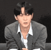 a young man wearing a gray jacket and a white shirt is sitting on a couch and making a funny face .