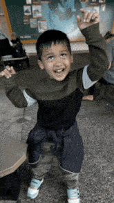 a young boy with his arms in the air is standing in front of a chalkboard