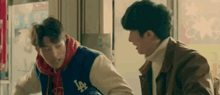 two young men are talking to each other in a store . one of the men is wearing a baseball jacket .