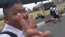 a young boy in a school uniform is making a peace sign with his hands .