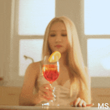 a woman is sitting at a table holding a glass of wine with a lemon slice on it