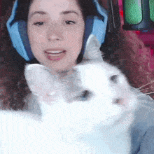 a woman wearing headphones is petting a white cat while sitting in front of a microphone .