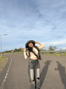 a woman wearing a cowboy hat and ripped jeans stands on a road