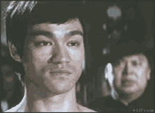 bruce lee is looking at the camera with a man in a police hat in the background .