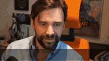a man with a beard is sitting in front of an orange chair with a world of warcraft poster in the background