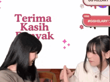 two girls are giving each other a fist bump in front of a sign that says terima kasih