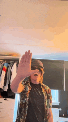 a man wearing sunglasses and a hat is covering his face with his hand .