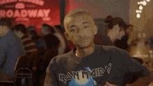 a man wearing a iron maiden t-shirt is sitting at a table in front of a crowd of people .