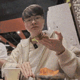 a young man wearing glasses is sitting at a table eating food .