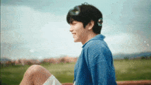 a young man is sitting on a bench in a field with soap bubbles coming out of his ears .