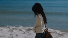 a woman is walking on the beach with a brown bag