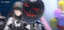 a girl is standing next to a large black ball with a red face on it .