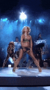 a woman in a green bikini is dancing on a stage with other dancers