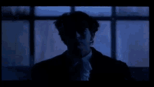 a man in a suit is standing in front of a window in a dark room