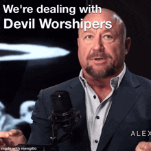 a man in a suit speaking into a microphone with the words we 're dealing with devil worshippers above him