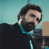 a man with a beard wearing a suit and tie has a netflix logo on the bottom right