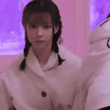 a young woman in a white coat is waving her hand in front of a pink wall .