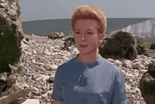 a woman in a blue dress stands on a rocky beach near the ocean