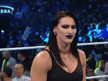 a woman in a black tank top is standing in a wrestling ring looking at the camera