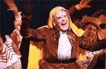 a group of people are dancing on a stage and one of them is wearing a yellow cape