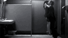 a black and white photo of a man and woman kissing in a bathroom .