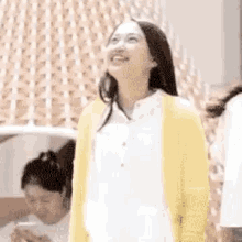 a woman in a yellow cardigan is smiling and looking up .