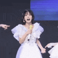 a young woman in a white dress is singing into a microphone .