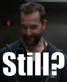a man with a beard is smiling in front of a sign that says still ?