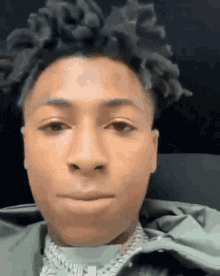 a close up of a young man 's face with dreadlocks and a necklace .