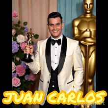 a man in a tuxedo is holding an oscar statue in front of a statue of juan carlos