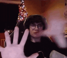 a man wearing glasses and headphones is sitting in front of a christmas tree and making a funny face .