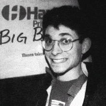 a man wearing glasses is smiling in front of a big b sign