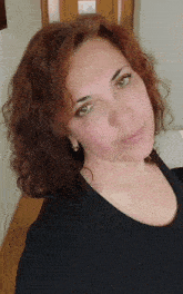a woman with red hair and green eyes is wearing a black shirt and earrings