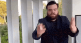 a man with a beard is standing in front of a balcony with his hands up .