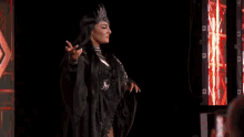 a woman in a black dress and crown is standing on a stage in front of a crowd .