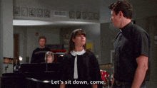 a man and a woman are standing next to each other and the woman is saying let 's sit down come