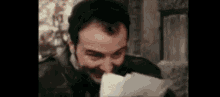 a man with a beard is holding a piece of paper in his mouth and laughing .